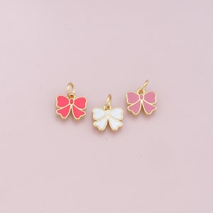 May include: Three gold bow charms with enamel paint. The bows are pink, white, and red.