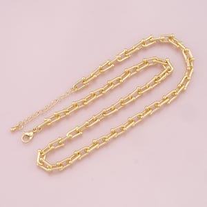 May include: A gold chain necklace with a unique link design. The chain is made of small, round links that are connected together in a pattern that resembles a series of small, interlocking circles.
