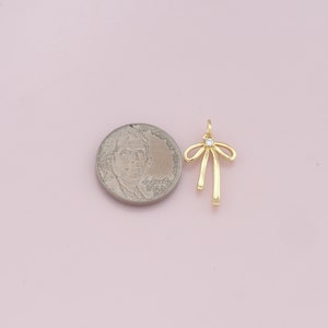 May include: Gold-toned bow charm with a clear rhinestone in the center. The charm is about the size of a US quarter.