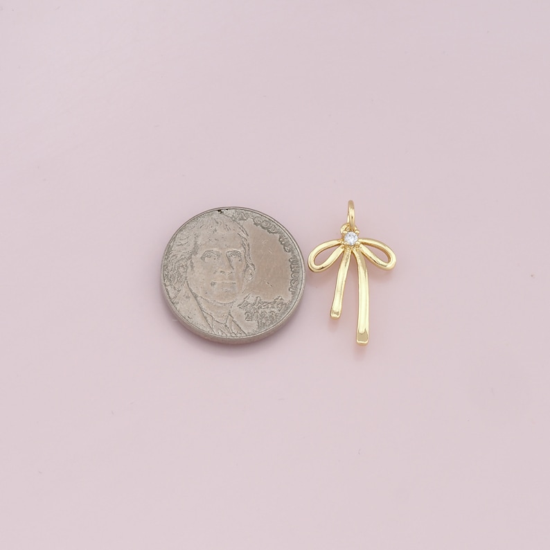 May include: Gold-toned bow charm with a clear rhinestone in the center. The charm is about the size of a US quarter.