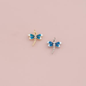 May include: Two dragonfly charms. One is gold-toned, the other silver-toned. Both have white and blue enamel wings and a clear crystal body. The dragonfly charms are small and delicate, perfect for jewelry making.