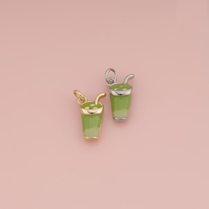 May include: Two small charms shaped like drinking glasses filled with a green beverage. One charm is gold-toned with a light green enamel fill, and the other is silver-toned with a similar green enamel design, both featuring a small straw.