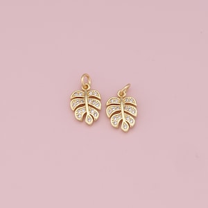 May include: Two gold-tone leaf charms with clear crystal accents. The leaves are detailed with a delicate, intricate design.