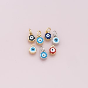 Könnte beinhalten: Sortiment von sieben kleinen bösen Augen-Anhängern mit goldenen und silbernen Einstellungen. Die Anhänger sind blau, schwarz, rot und türkis mit weißen Zentren.
