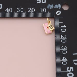 May include: A gold-colored charm in the shape of a pink envelope with a red heart and a small tag that says "I love you." The charm is likely for a necklace or bracelet.