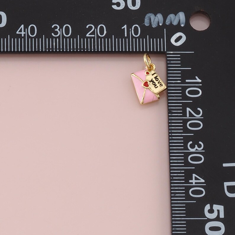 May include: A gold-colored charm in the shape of a pink envelope with a red heart and a small tag that says "I love you." The charm is likely for a necklace or bracelet.