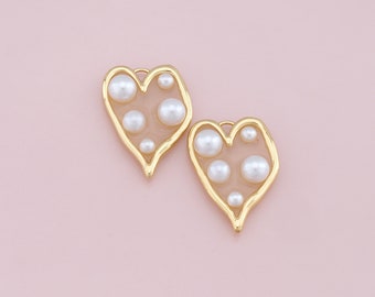 May include: A pair of gold heart-shaped earrings with a translucent pink background and white pearl accents.