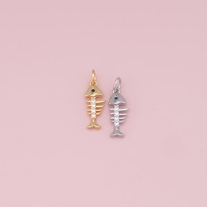 May include: Two fish bone charms, one gold and one silver, with black eyes and clear crystal accents.