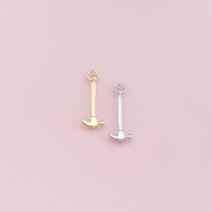 May include: Two hammer charms, one gold and one silver, on a pink background.