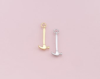 May include: Two hammer charms, one gold and one silver, on a pink background.