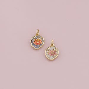 Könnte beinhalten: Zwei goldfarbene Anhänger mit Blumenmotiv. Ein Anhänger hat einen blauen Hintergrund mit einer roten Blume und der andere Anhänger hat einen weißen Hintergrund mit einer rosa Blume.