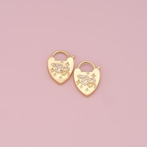 May include: A pair of gold heart-shaped earrings with a snake and star design. The earrings are made of metal and have a shiny finish.