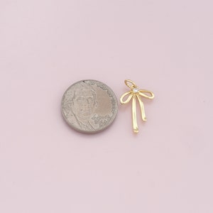 May include: Gold-toned bow charm with a clear rhinestone in the center. The charm is about the size of a US dime.