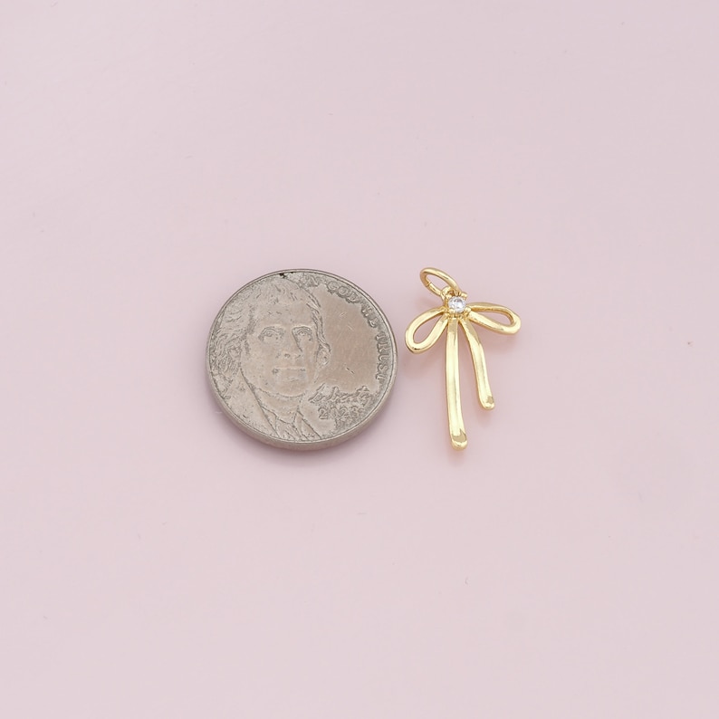 May include: Gold-toned bow charm with a clear rhinestone in the center. The charm is about the size of a US dime.