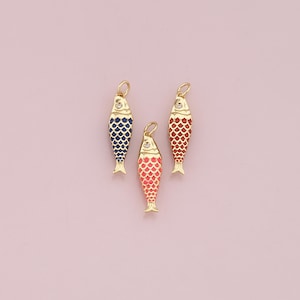 May include: Three gold fish charms with coloured scales. One charm has blue scales, another has red scales, and the third has coral scales. Each charm has a small, clear gem and a loop for hanging.