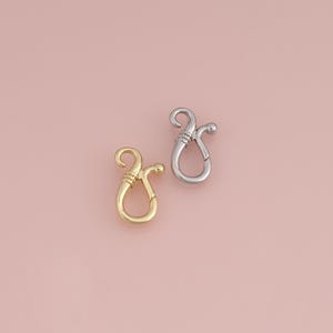 May include: Two jewellery clasps, one in a gold tone and one in a silver tone. Each clasp features a curved, hook-like design with a spring-loaded mechanism and a small ball detail at the end of the arm, providing a secure closure for necklaces.