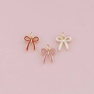 May include: Three gold-colored bow charms with enamel accents. The bows are red, pink, and white.