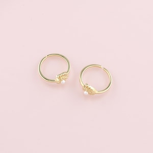 May include: Two gold hoop earrings with a pearl and a leaf design.