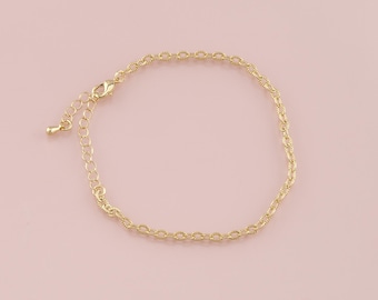 May include: A gold-colored bracelet with a delicate chain design. The bracelet features an adjustable length with a lobster clasp closure. The jewelry is displayed on a light pink background.