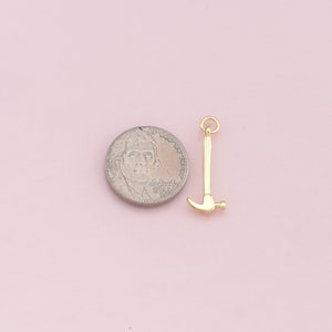 May include: Gold-toned hammer charm pendant, shown next to a US quarter for size comparison.