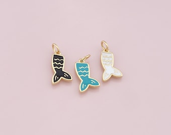 Puede incluir: Tres colgantes de cola de sirena en negro, turquesa y blanco con bordes dorados. Cada colgante tiene un lazo en la parte superior para sujetarlo a la joyería. Los colgantes están sobre un fondo rosa claro.