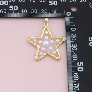 Pu&ograve; includere: Un ciondolo a forma di stella dorata con un bordo strutturato e un centro trasparente pieno di piccole perle bianche. Il ciondolo ha un anello nella parte superiore per una catena. La forma a stella &egrave; popolare per i gioielli.
