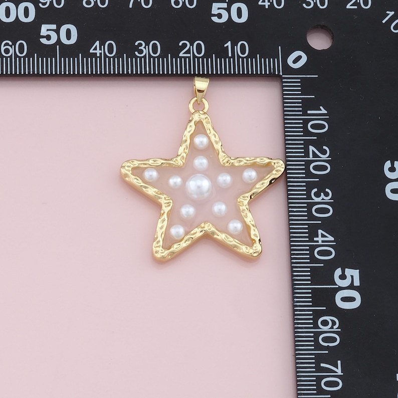 Pu&ograve; includere: Un ciondolo a forma di stella dorata con un bordo strutturato e un centro trasparente pieno di piccole perle bianche. Il ciondolo ha un anello nella parte superiore per una catena. La forma a stella &egrave; popolare per i gioielli.