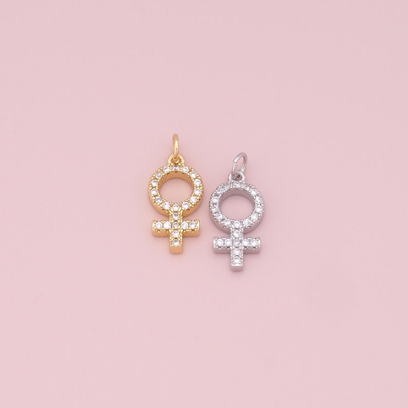 May include: Two silver and gold charms in the shape of the female symbol, both with clear crystal accents.
