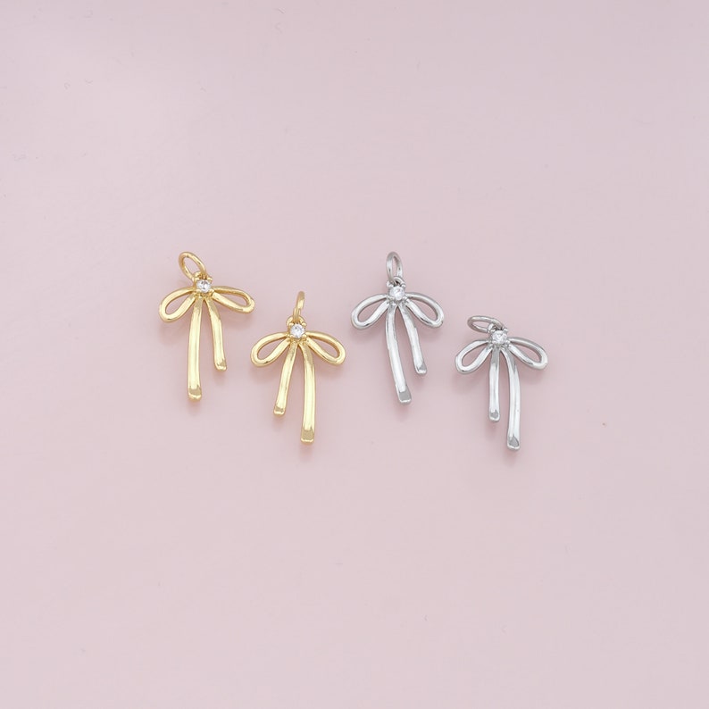 May include: Three gold and silver bow charms with a clear rhinestone in the center. The charms are perfect for adding a touch of elegance to jewelry projects.