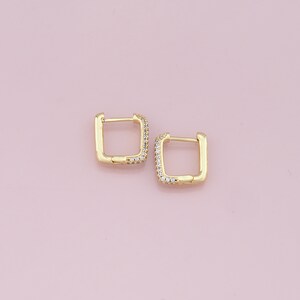 May include: A pair of gold square hoop earrings with small clear cubic zirconia stones around the edge.