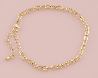 May include: A gold-colored anklet with an oval link chain design. The anklet features a lobster clasp closure and an adjustable chain for a customized fit. The jewelry is displayed on a light pink background.