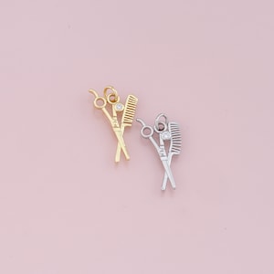 May include: Two gold and silver charms in the shape of crossed scissors and a comb. Each charm has a small clear rhinestone in the center.