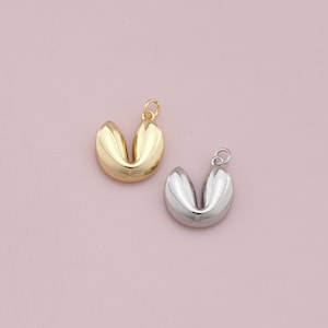 Pode incluir: Dois pingentes de biscoito da sorte, um dourado e outro prateado. Os pingentes têm a forma de um biscoito da sorte e têm um furo na parte superior para serem presos a um colar ou pulseira.