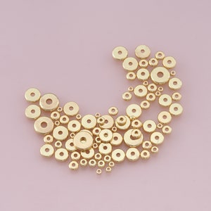 May include: A collection of gold-colored metal jump rings of various sizes, scattered on a pink background.