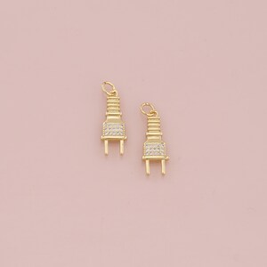May include: Two gold-tone plug charms with clear crystal accents. The charms are shaped like electrical plugs and have a shiny finish.