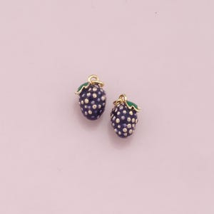 May include: Two gold-colored charms shaped like blackberries with green leaves. The blackberries have a textured surface and are decorated with small white dots.