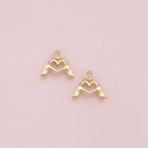 Può includere: Due ciondoli dorati a forma di mani che formano un cuore. I ciondoli hanno un anello in cima per essere attaccati a un braccialetto o una collana.