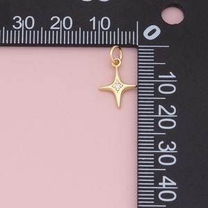 May include: Gold star charm with a small clear rhinestone in the center. The charm is about 1 cm wide and is shown next to a ruler.