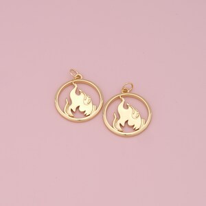 Könnte beinhalten: Zwei goldfarbene Metallanhänger in Form eines Kreises mit einem Flammenmotiv im Inneren.