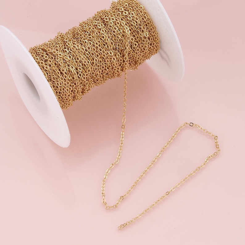K&ouml;nnte beinhalten: Eine Spule mit goldfarbener Kette, wobei ein St&uuml;ck Kette auf einer rosa Oberfl&auml;che liegt.