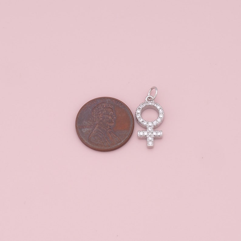 May include: A silver charm in the shape of the female symbol, with small clear stones set around the edges.