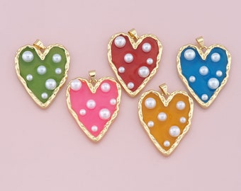 May include: Five heart-shaped pendants in green, red, pink, blue, and orange. Each pendant has a gold-colored border and is filled with white pearls. The pendants are on a light pink background.