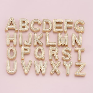 May include: Gold-tone alphabet letter charms with clear cubic zirconia stones. Each letter is individually crafted and features a detailed design.