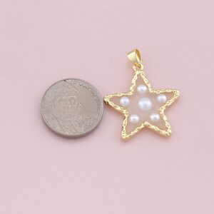 Pu&ograve; includere: Ciondolo a forma di stella color oro con centro rosa chiaro e perle finte. Il ciondolo ha un bordo dorato strutturato e un piccolo anello per una catena. Una moneta &egrave; accanto al ciondolo per il confronto delle dimensioni.
