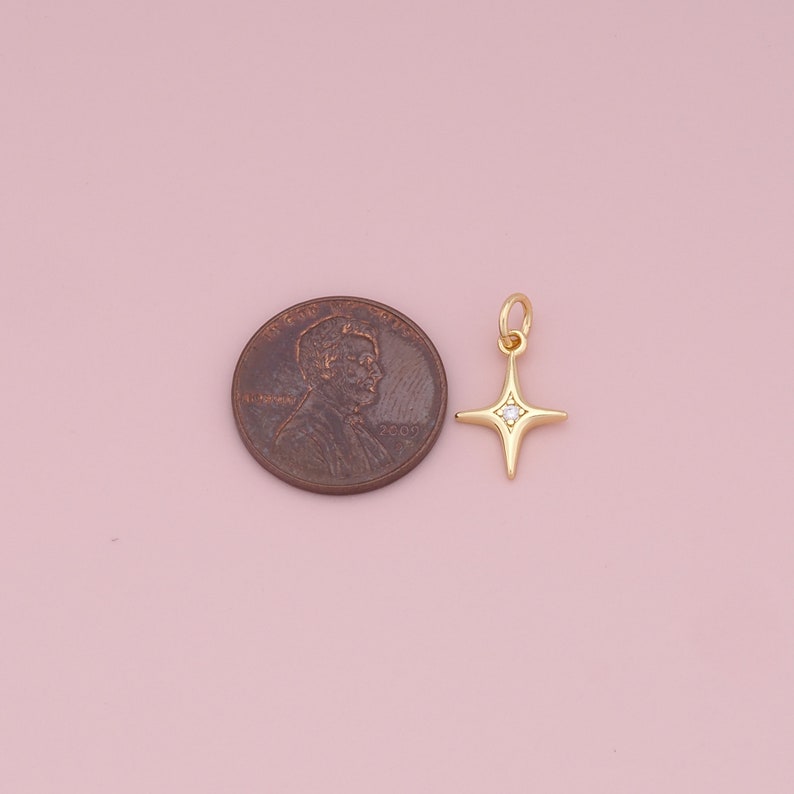 May include: Gold star charm with a single clear rhinestone in the center. The charm is about the size of a US penny.