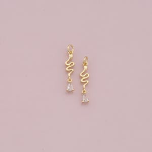 May include: A pair of gold earrings with a dangling, wavy design and a clear pear-shaped stone at the end of each earring.