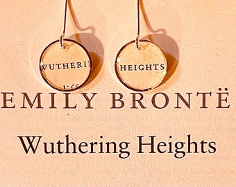 May include: A pair of circular drop earrings featuring the text WUTHERING and HEIGHTS on each disc. The earrings are displayed above the printed text EMILY BRONTË and Wuthering Heights on a light-colored background.