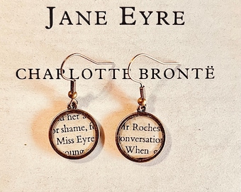 May include: A pair of round bronze-toned earrings featuring circular inserts of printed book text from Jane Eyre by Charlotte Brontë. The earrings have simple metal hooks and display snippets of black text on a cream-colored paper background.