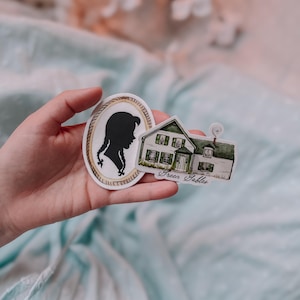 May include: Two stickers, one featuring a silhouette of a girl with braids in a gold oval frame and the other a green house with white trim and the text "Green Gables".