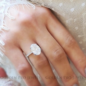 May include: A silver ring with a large oval-shaped diamond set in a pave setting. The ring is on a person's finger.